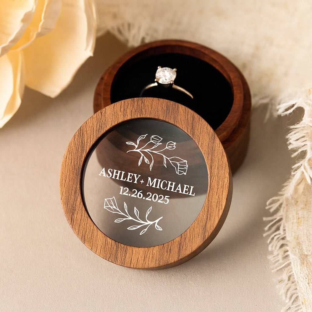 Wooden ring box with engraved names and date holding diamond engagement ring..