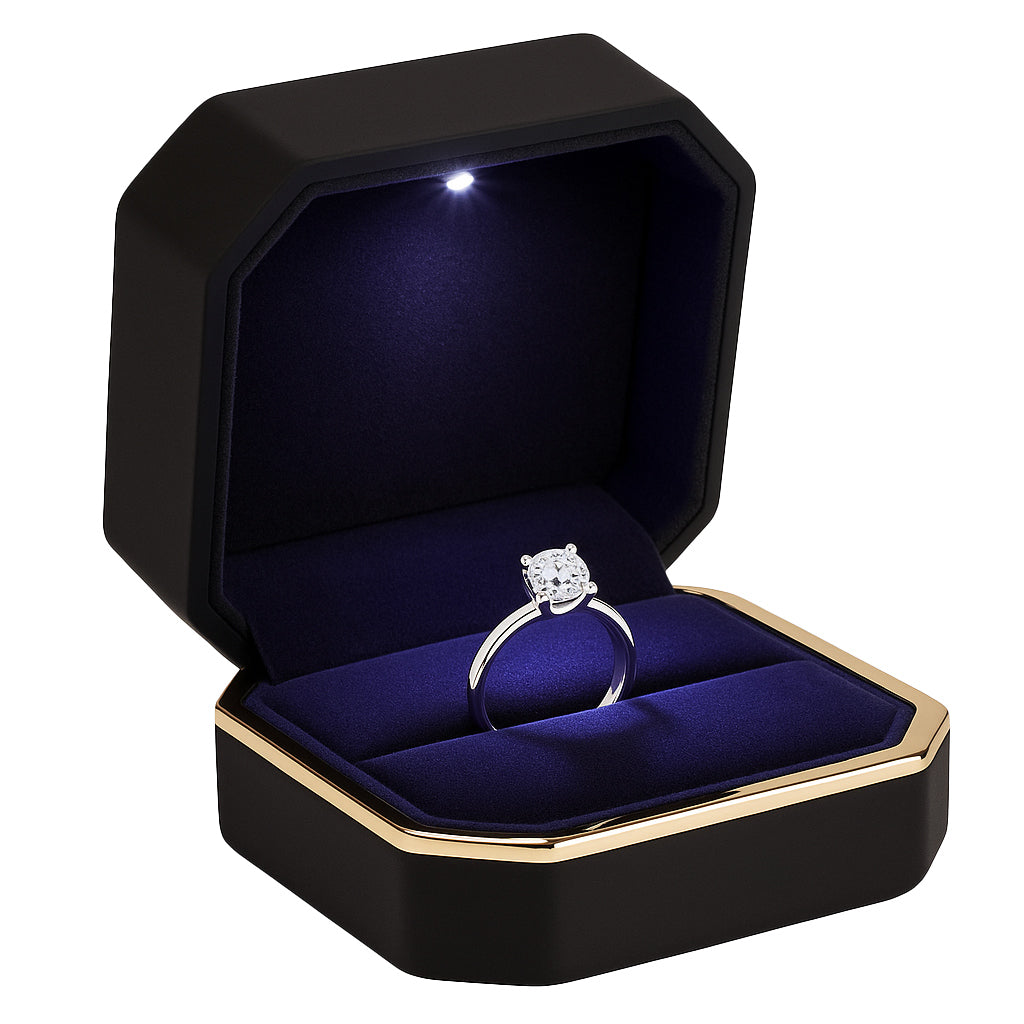 Open black matte ring box with gold trim and LED light holding diamond engagement ring